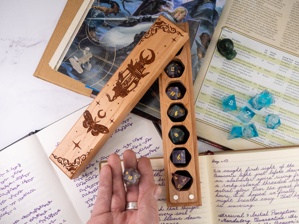 Wooden dice holder with engraved designs on a table with books and dice.