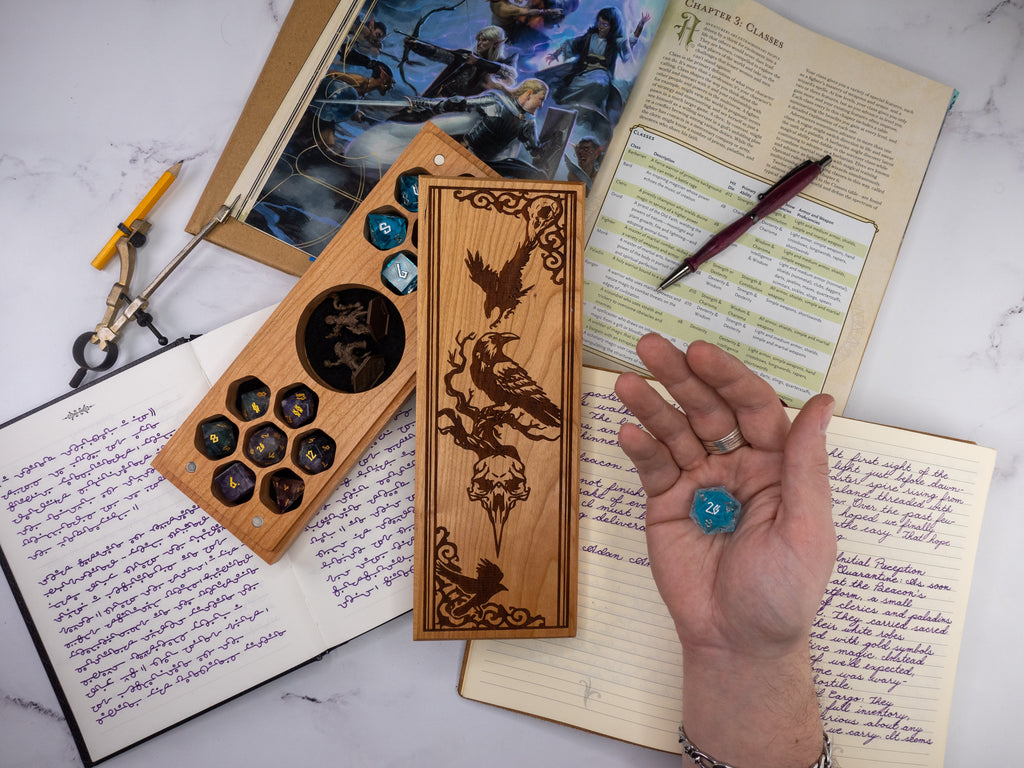 Wooden dice tray with engraved designs on a marble surface with books and a pen.