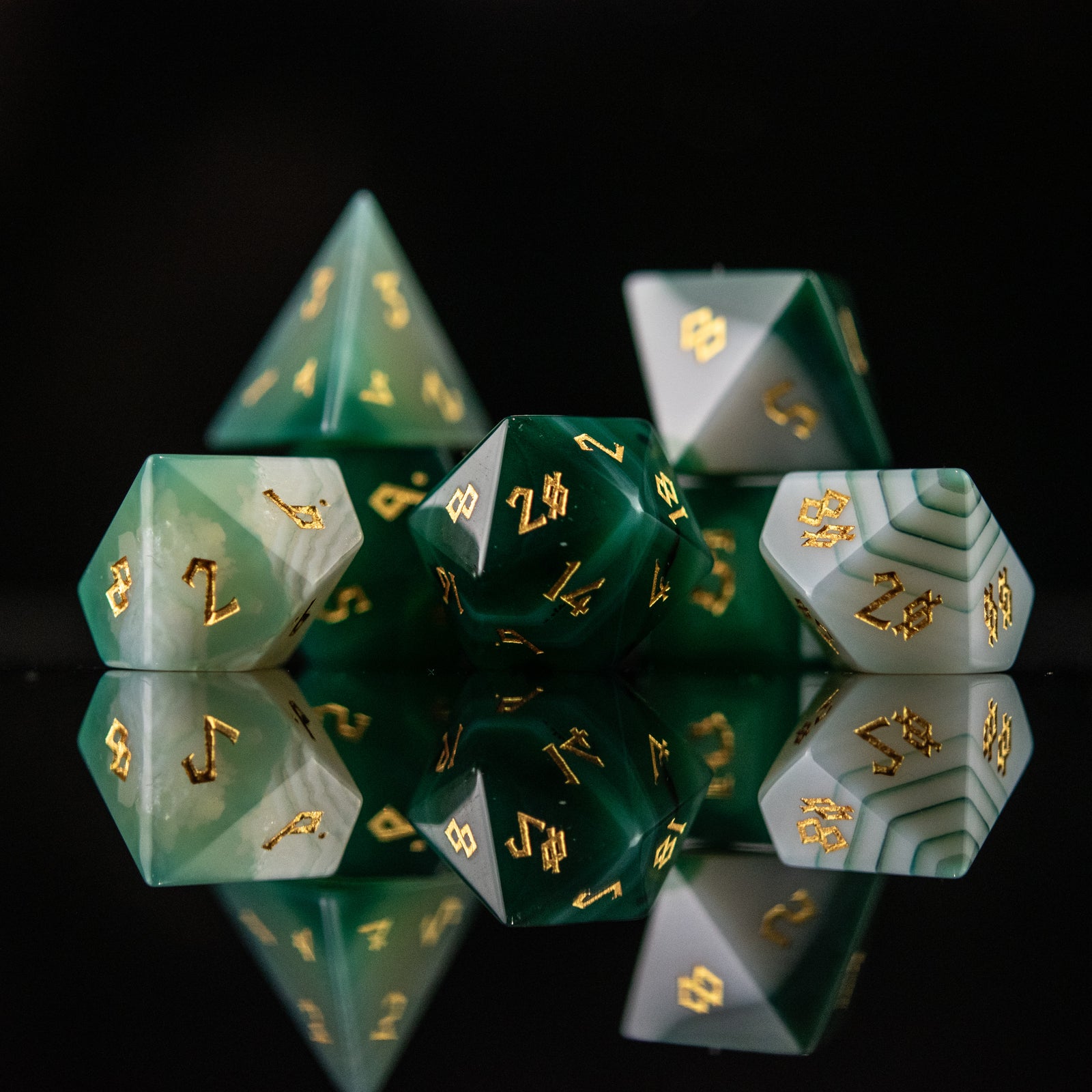 A set of green and white agate stone dice with engraved numbers, displayed on a reflective surface.