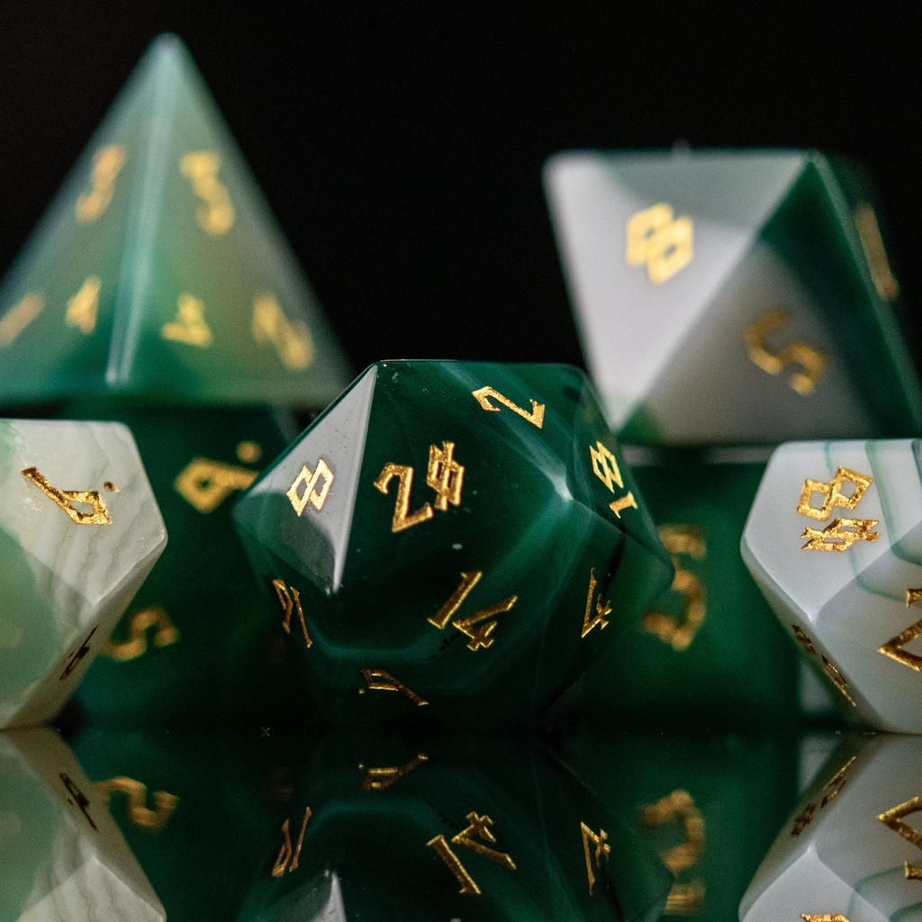 A set of green and white agate stone dice with engraved numbers, displayed on a reflective surface.