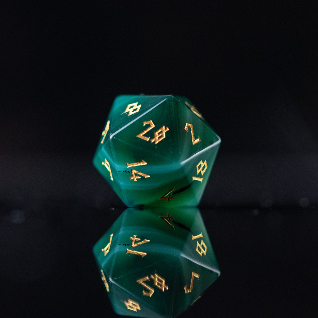 A set of green and white agate stone dice with engraved numbers, displayed on a reflective surface.