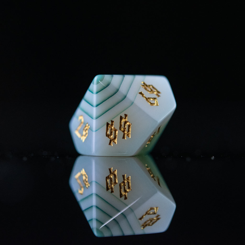 A set of green and white agate stone dice with engraved numbers, displayed on a reflective surface.