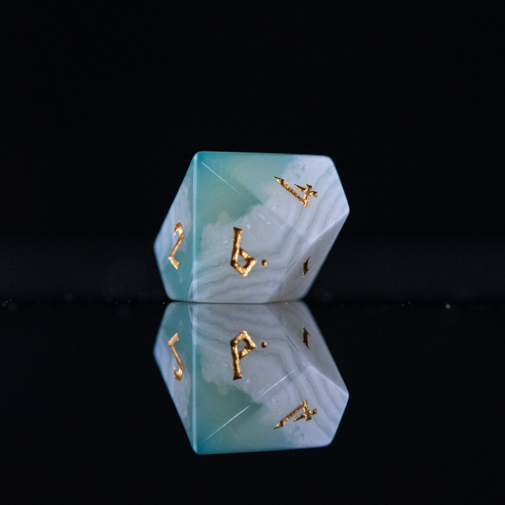 A set of green and white agate stone dice with engraved numbers, displayed on a reflective surface.