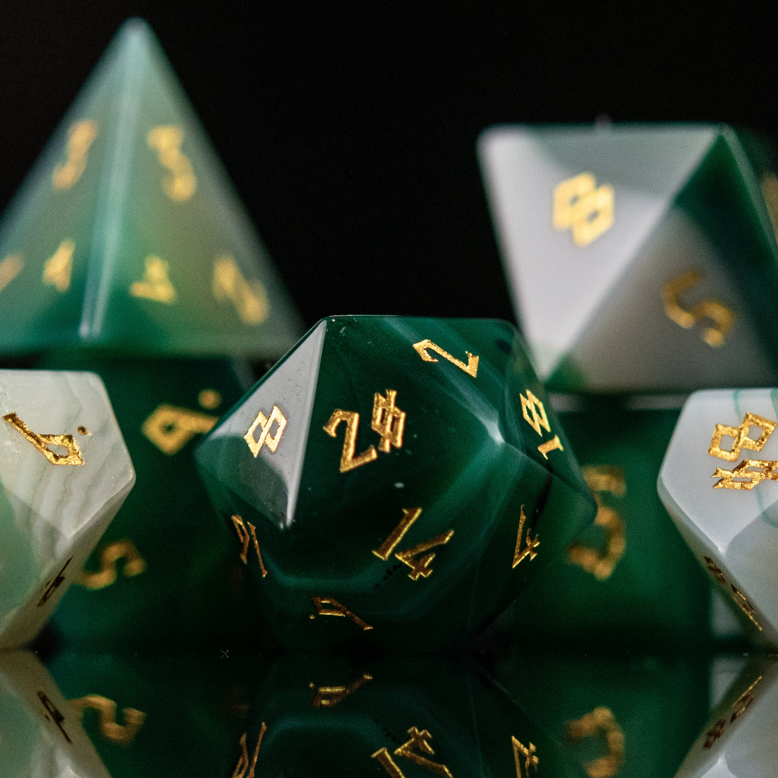 A set of green and white agate stone dice with engraved numbers, displayed on a reflective surface.