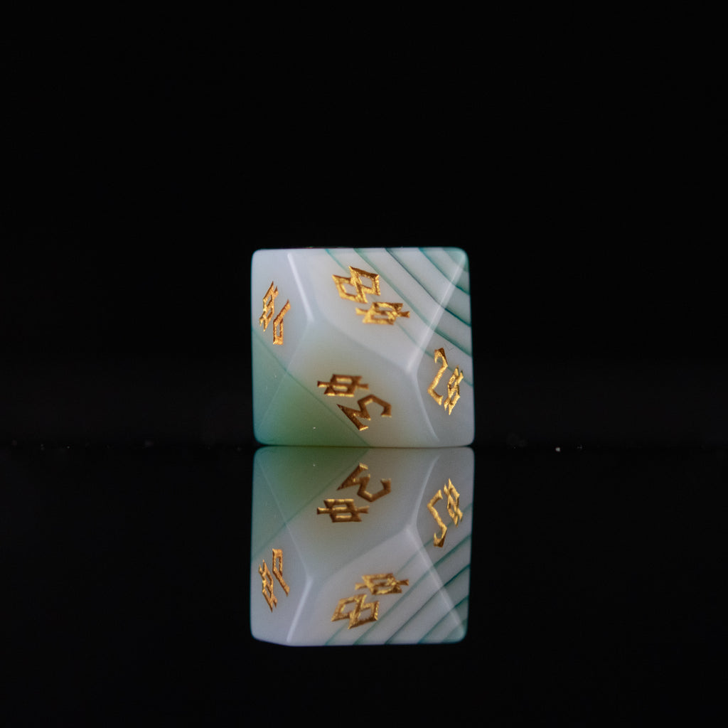 A set of green and white agate stone dice with engraved numbers, displayed on a reflective surface.