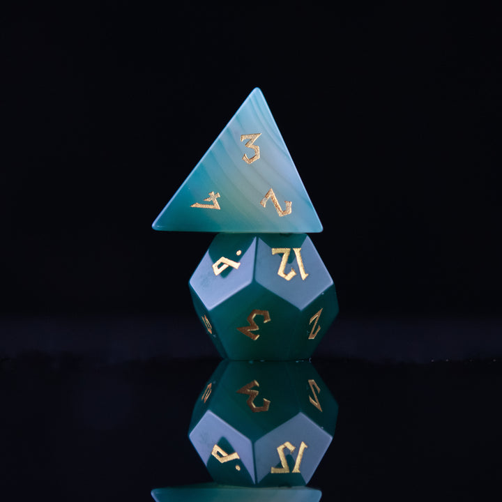 A set of green and white agate stone dice with engraved numbers, displayed on a reflective surface.