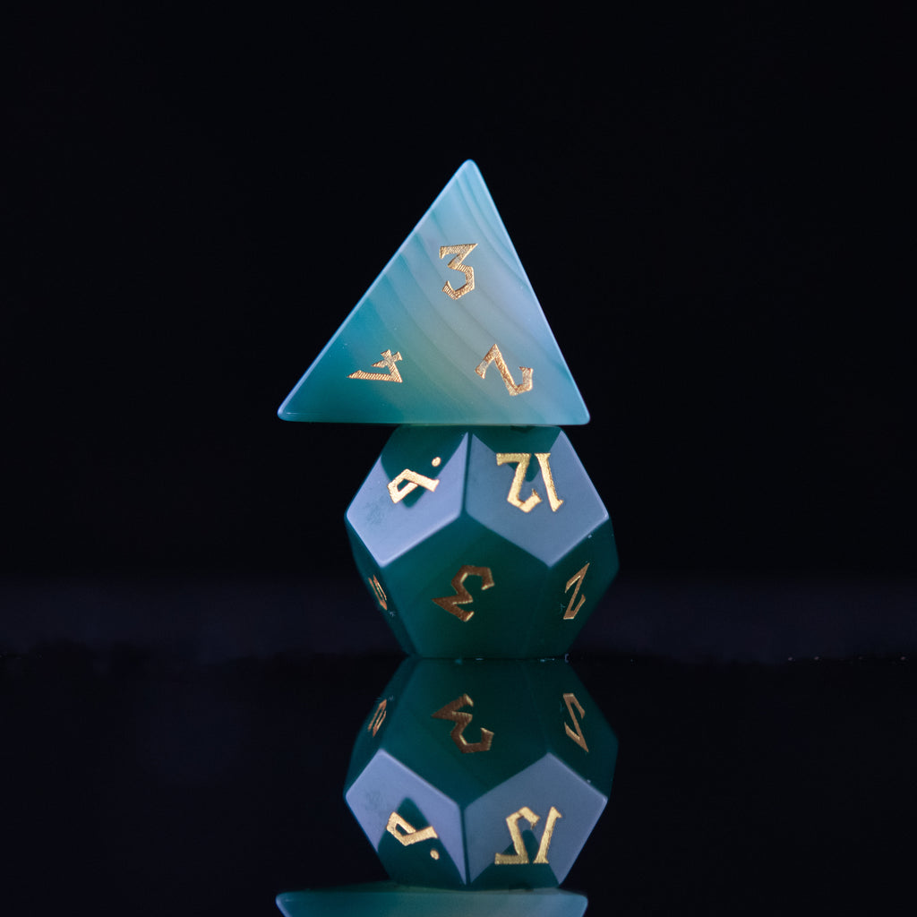 A set of green and white agate stone dice with engraved numbers, displayed on a reflective surface.