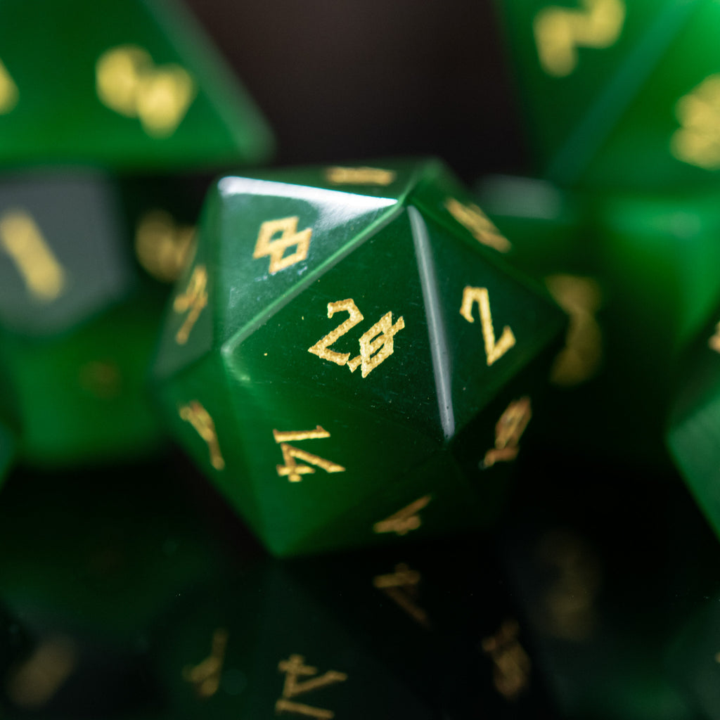 A collection of green cat's eye stone dice with engraved numbers, displayed against a dark background.