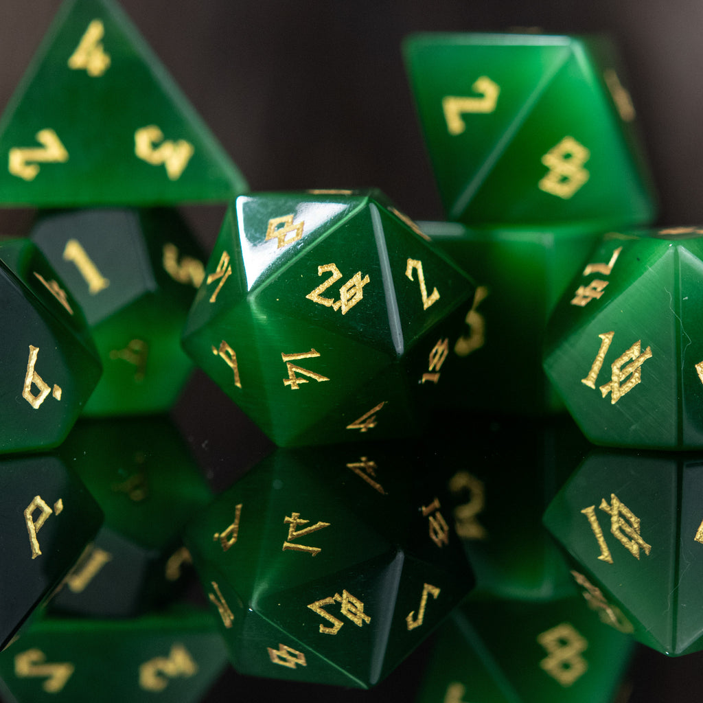 A collection of green cat's eye stone dice with engraved numbers, displayed against a dark background.