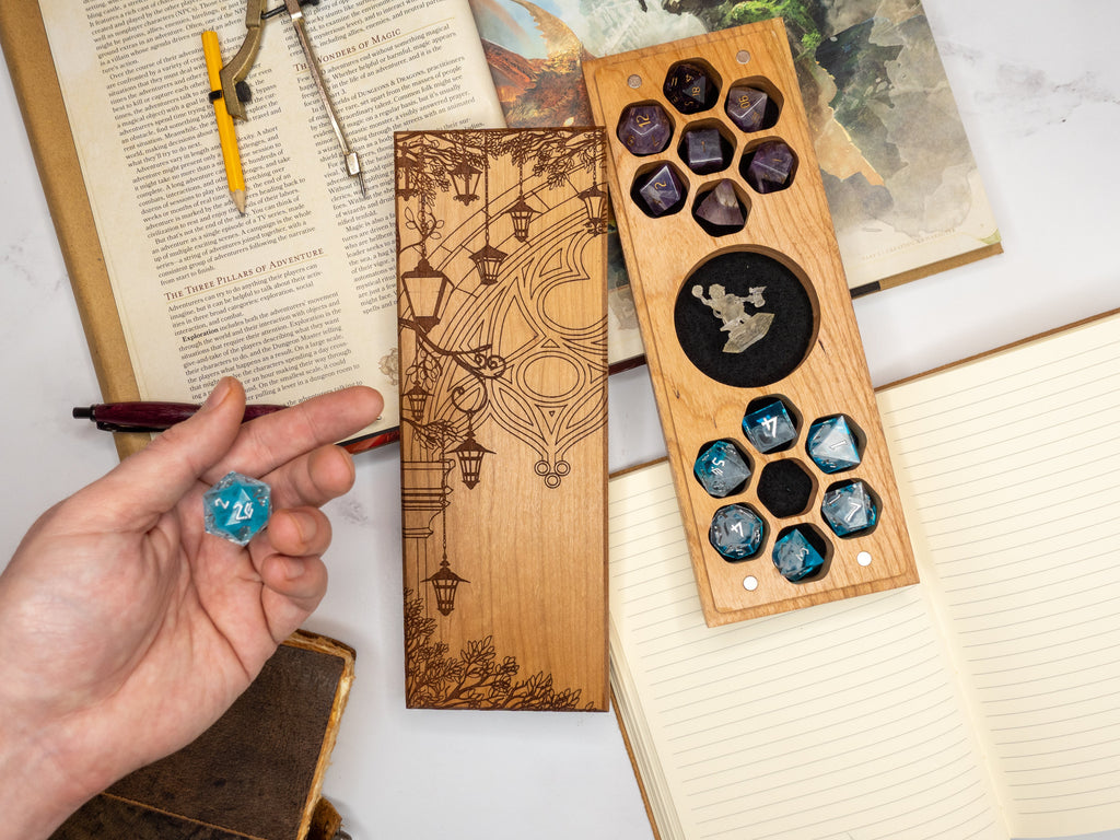 Hand holding a blue die next to wooden dice tray with engraved design on a book background