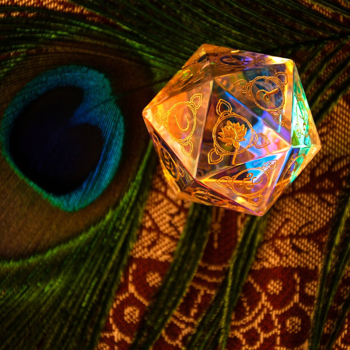 A multicolored prismatic glass d20 dice with Devanagari numerals, placed on a fabric with a peacock feather design, illuminated from below.
