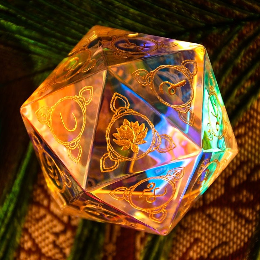 A multicolored prismatic glass d20 dice with Devanagari numerals, placed on a fabric with a peacock feather design, illuminated from below.