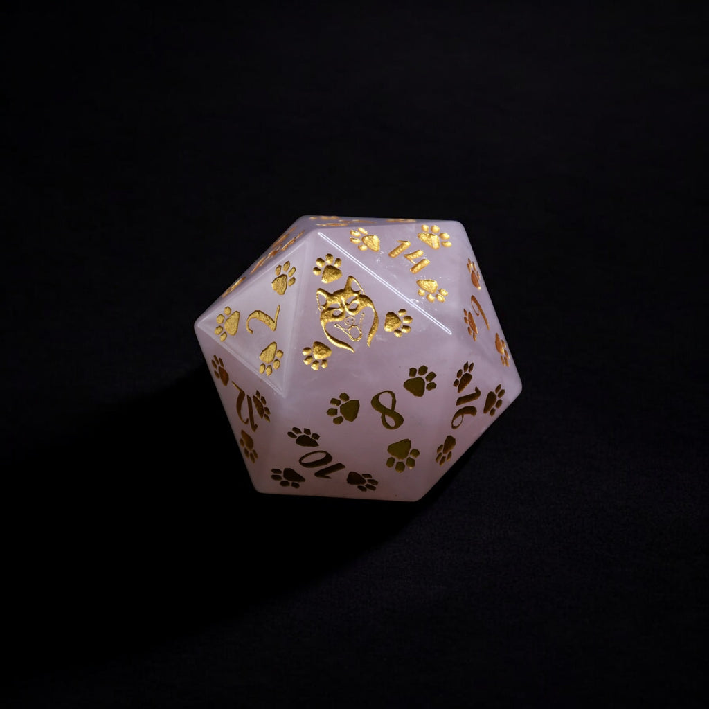 A pink rose quartz D20 dice with gold puppy paw prints and numbers engraved and painted on it