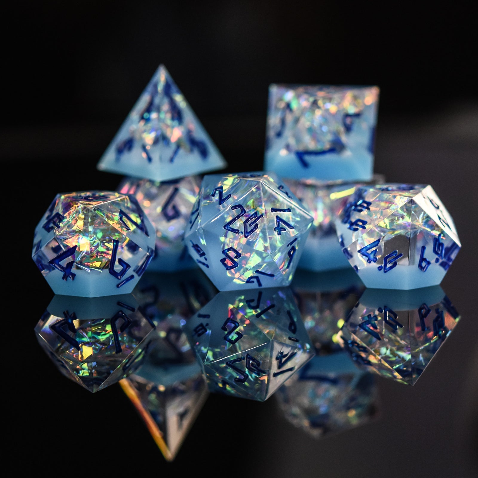 A set of sharp-edged, multicolored resin dice with engraved numbers, reflecting on a mirrored surface.