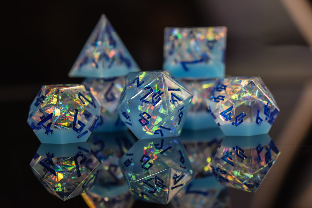 A set of blue iridescent sharp-edged, multicolored resin dice with engraved numbers, reflecting on a mirrored surface.