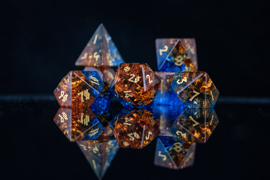 A set of hand-carved, shattered glass dice with engraved numbers, featuring a mix of blue and orange colors.