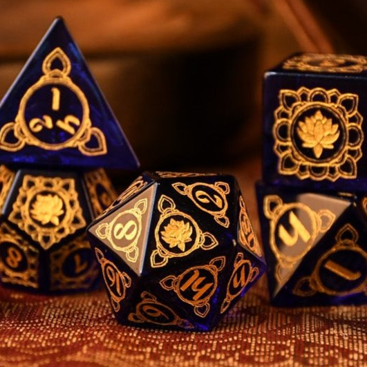 A set of hand-carved blue glass dice with golden designs, including a D4, D6, D8, D10, D12, and D20, displayed on a textured surface.