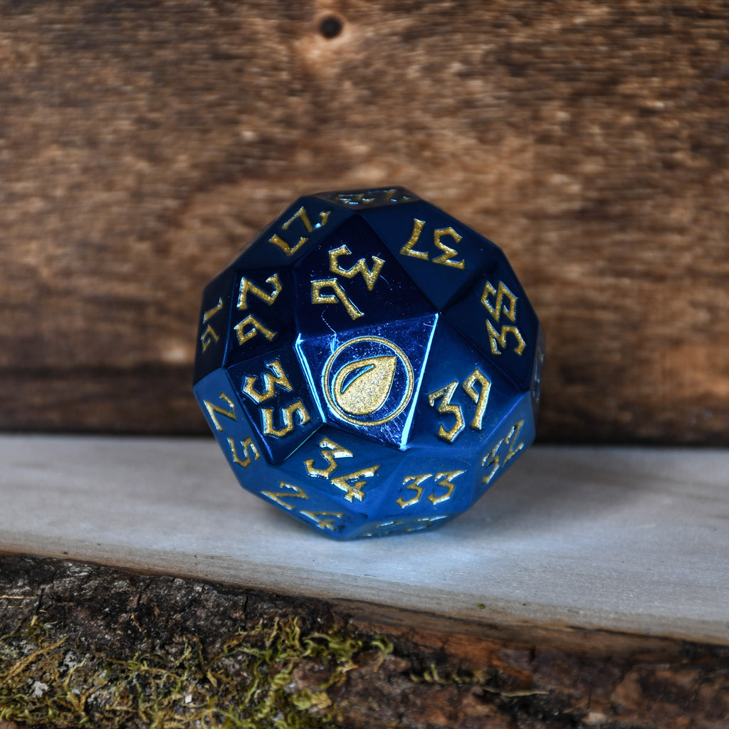 A single blue metal d40 spindown dice with gold numbers and iconography placed on a white surface with a wooden background.
