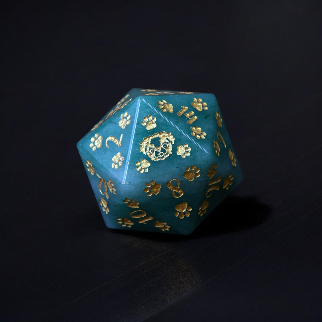 A green aventurine D20 dice with gold puppy paw prints and engravings
