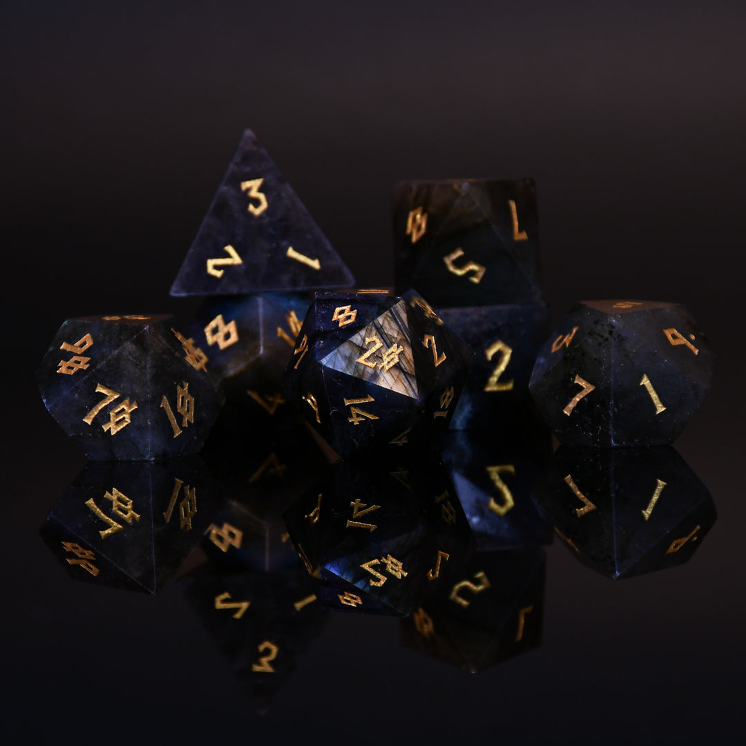 A collection of hand-carved, polished gemstone dice with engraved numbers, displayed on a dark background.