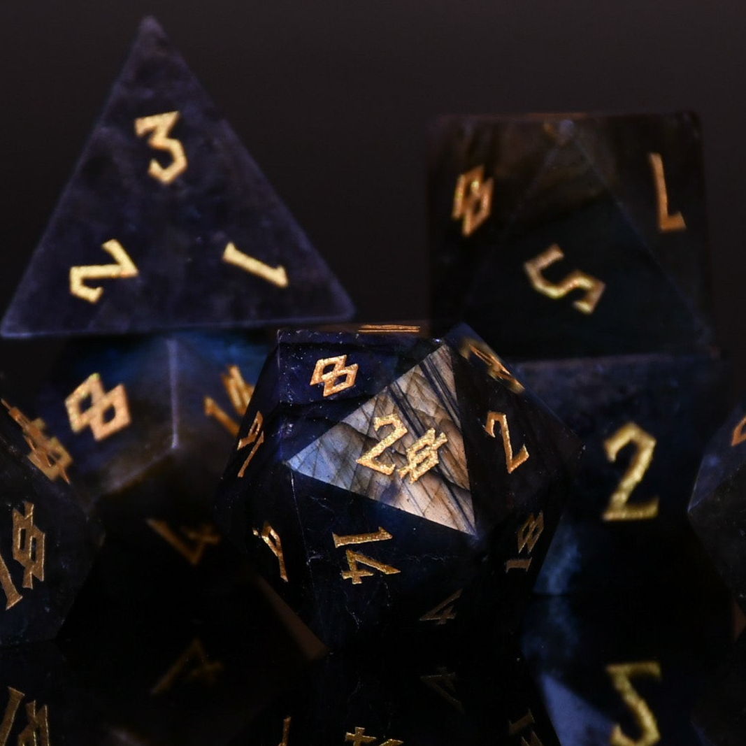 A collection of hand-carved, polished gemstone dice with engraved numbers, displayed on a dark background.