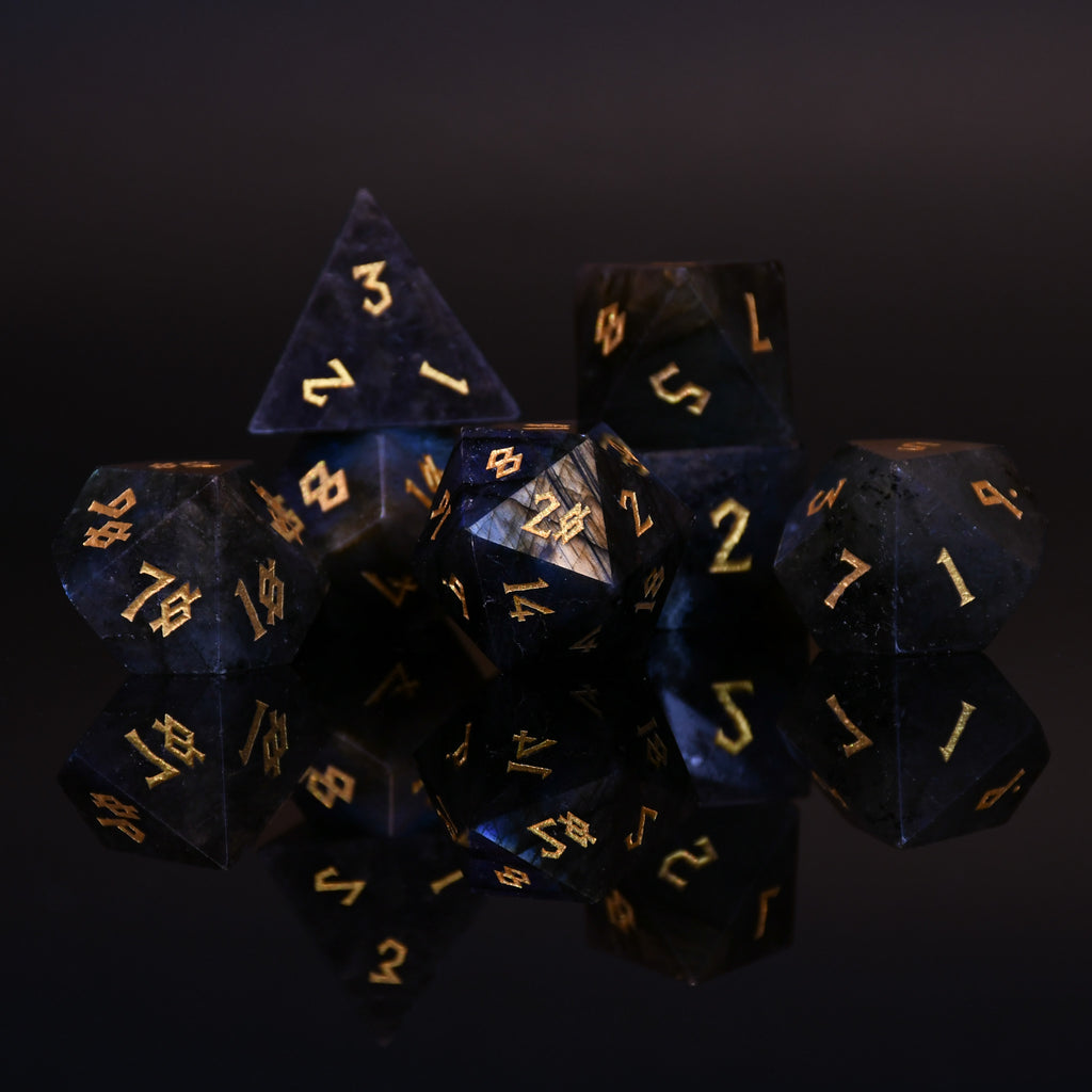 A collection of hand-carved, polished gemstone dice with engraved numbers, displayed on a dark background.