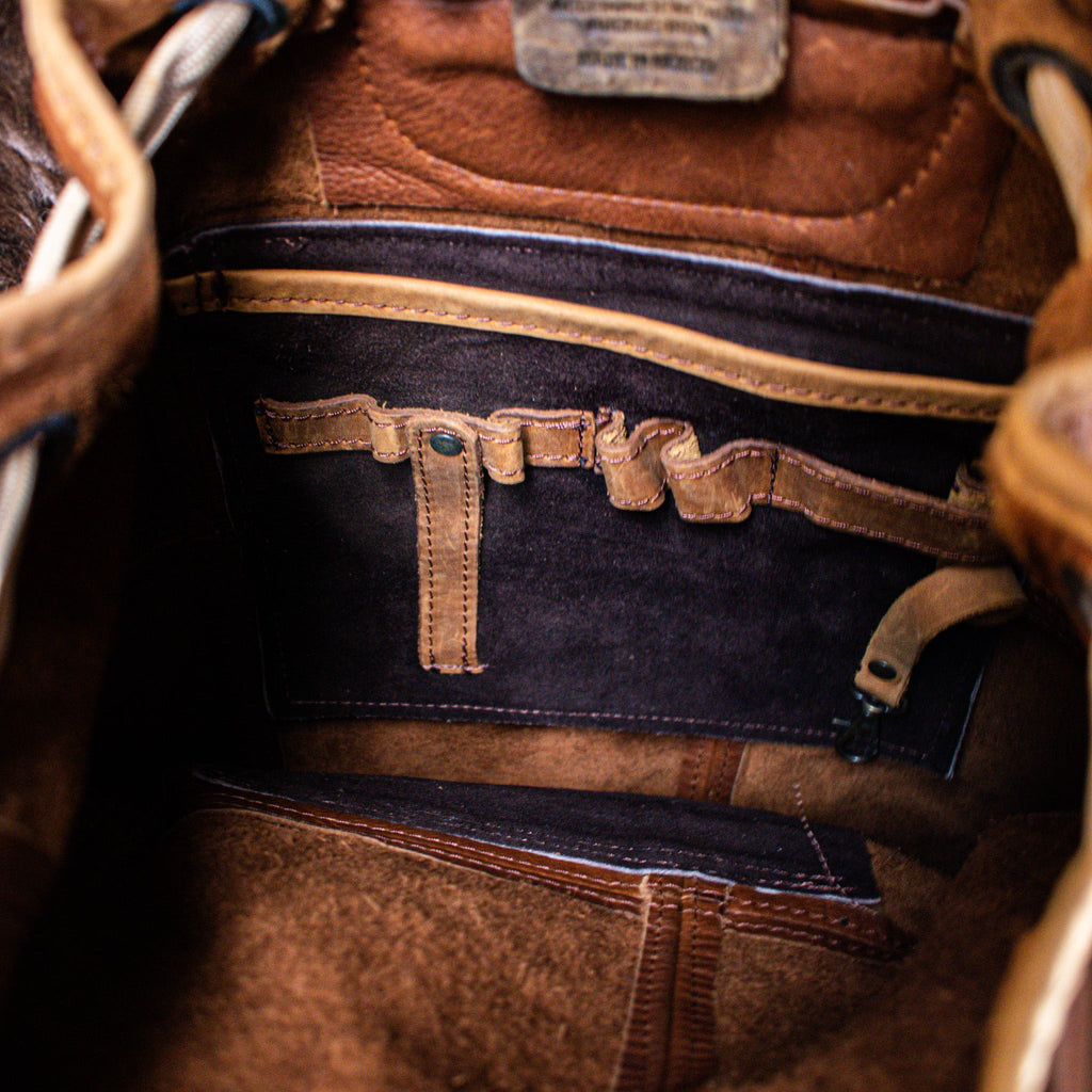 A brown leather bucket backpack with brass zippers and buckles, featuring multiple pockets and a cellphone holder.
