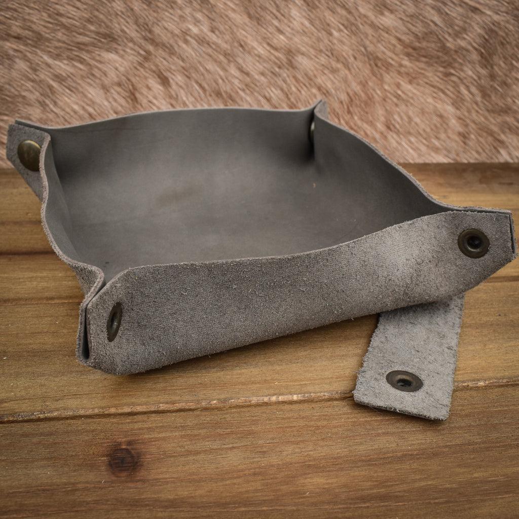 A grey leather collapsible dice tray on a wooden surface, with the tray unfolded next to its collapsed state.