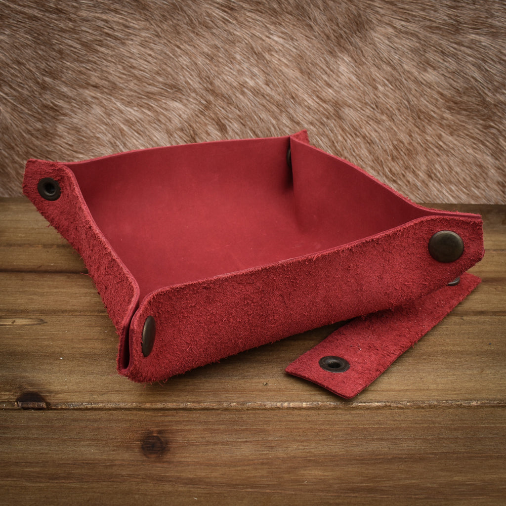 A red leather collapsible dice tray on a wooden surface, with the tray both folded and unfolded showing the compact and expanded states.