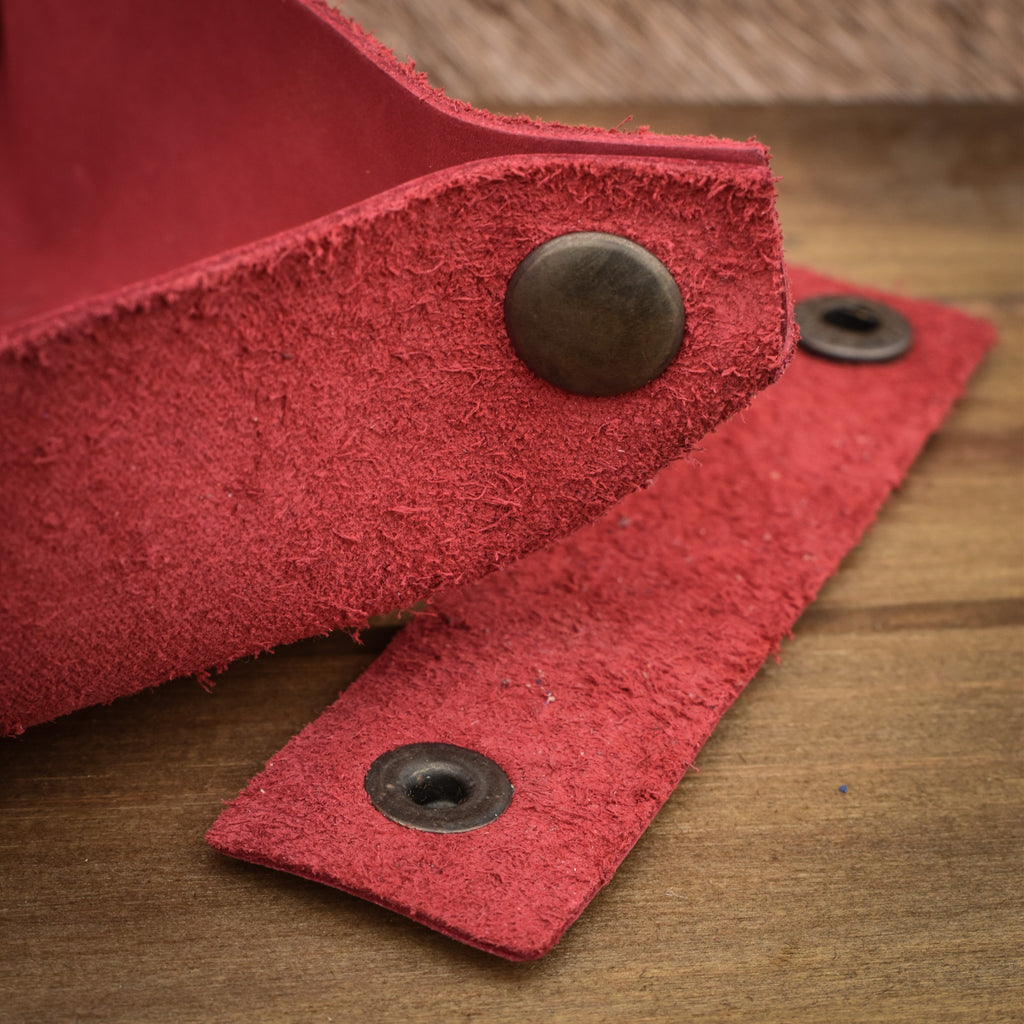 A red leather collapsible dice tray on a wooden surface, with the tray both folded and unfolded showing the compact and expanded states.