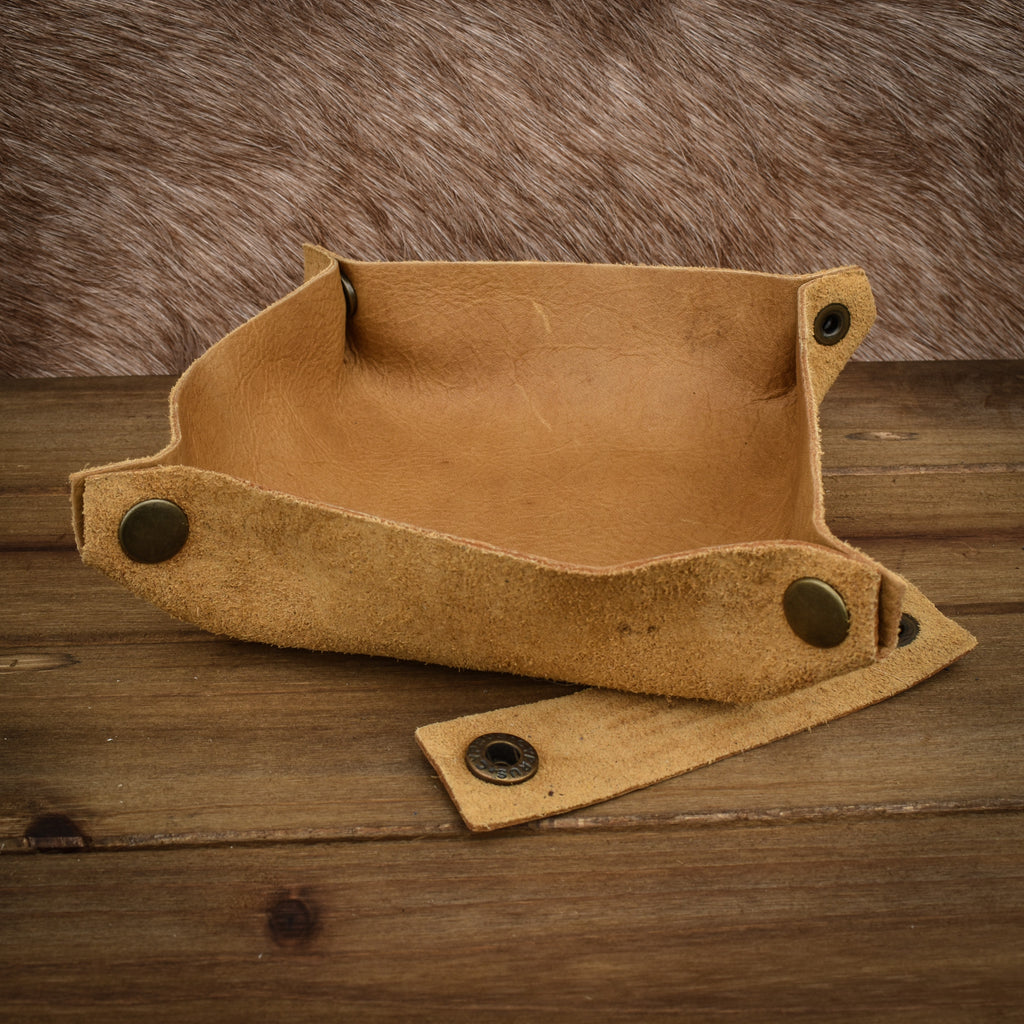 A textured tan leather dice tray with snap button closures, displayed on a wooden surface.