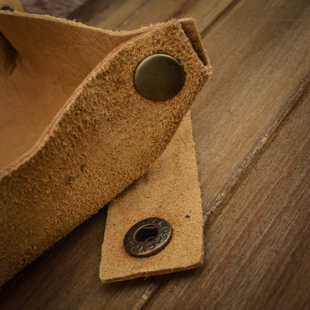 A textured tan leather dice tray with snap button closures, displayed on a wooden surface.