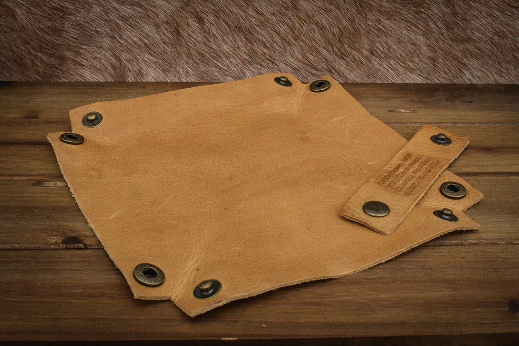 A textured tan leather dice tray with snap button closures, displayed on a wooden surface.