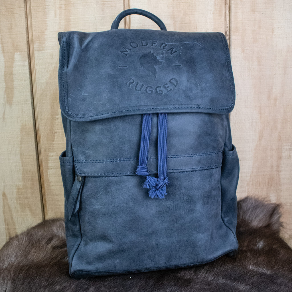 A navy-colored leather backpack with a front zipper pouch and two side pockets, featuring brass zippers and a drawstring top.