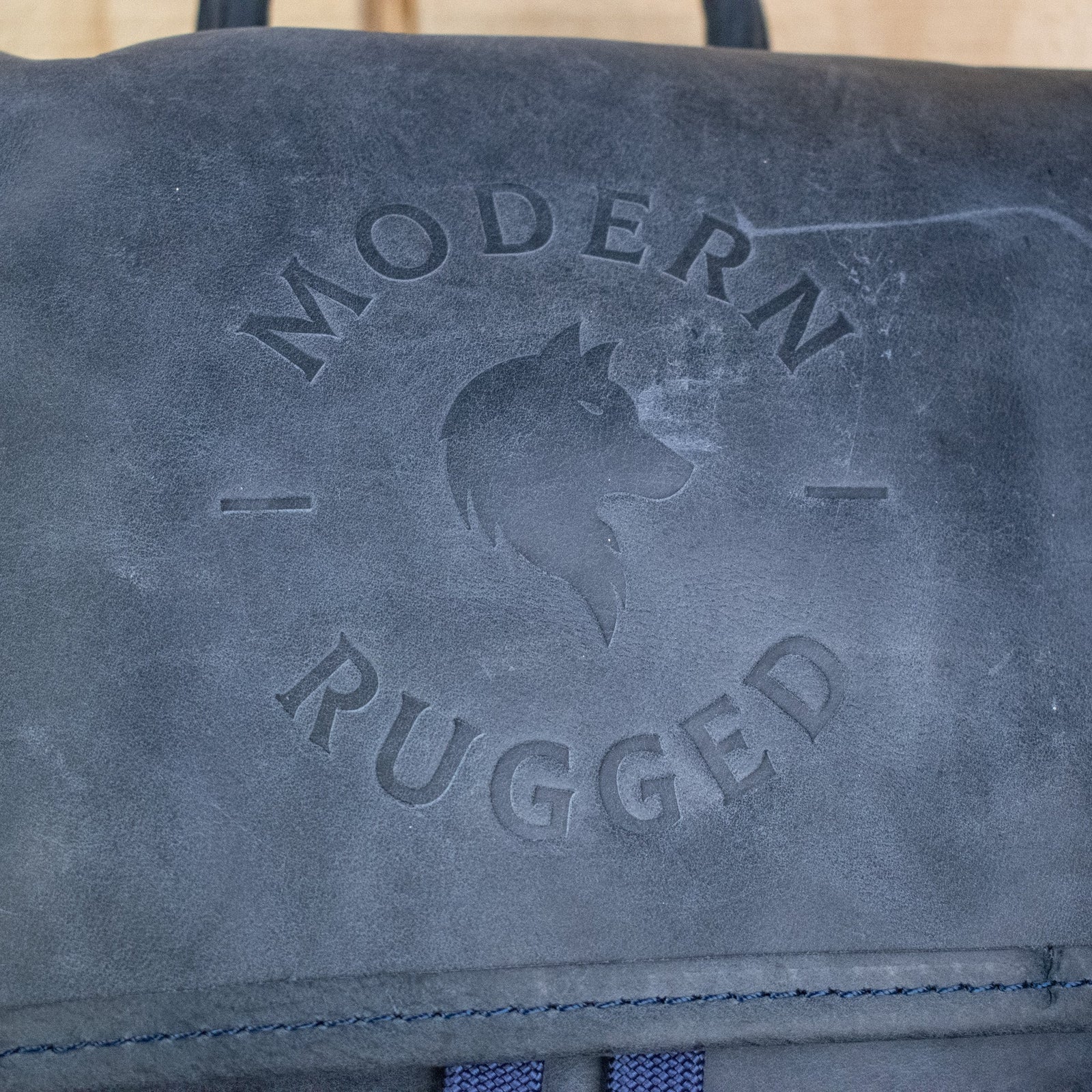 A navy-colored leather backpack with a front zipper pouch and two side pockets, featuring brass zippers and a drawstring top.