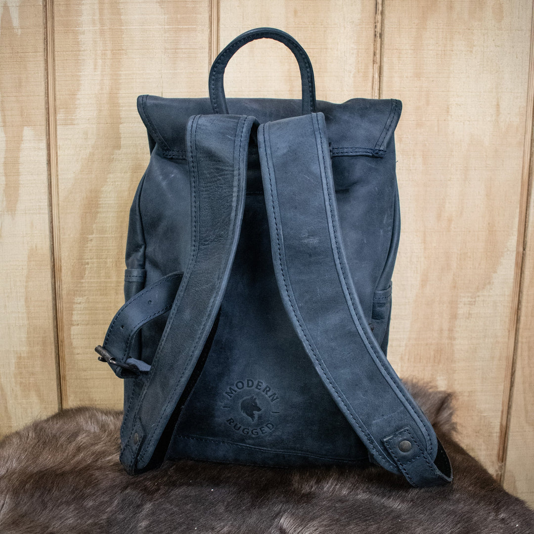 A navy-colored leather backpack with a front zipper pouch and two side pockets, featuring brass zippers and a drawstring top.