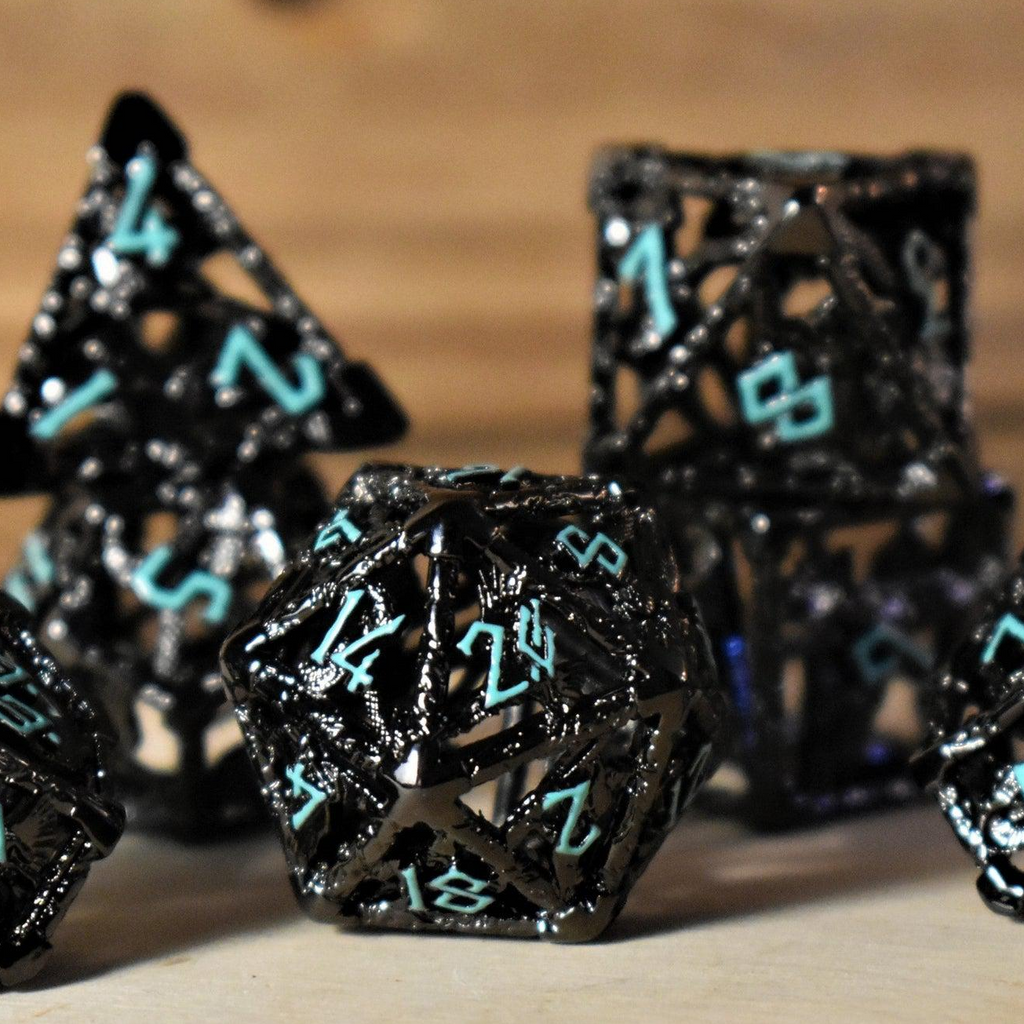 A set of hollow metal dice in black with blue embossed numbers, including various shapes such as a d4, d6, d8, d10, d12, and d20, displayed on a wooden surface.