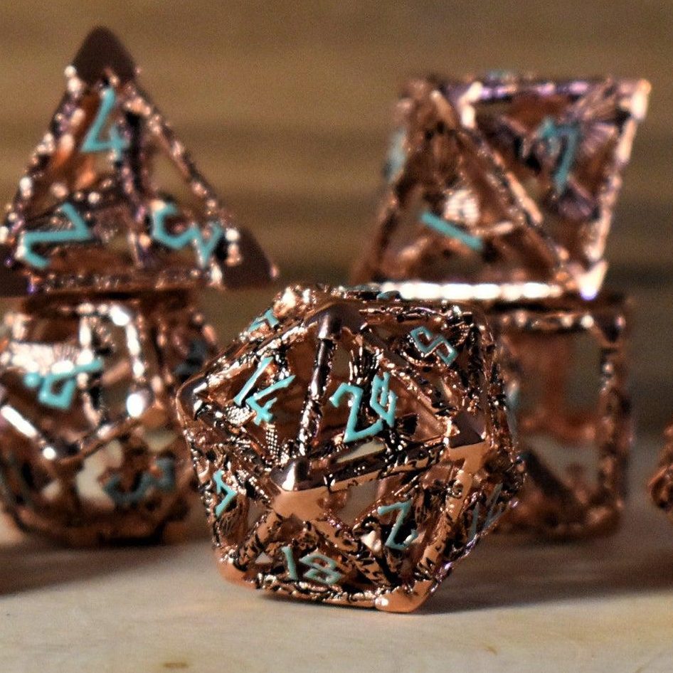 A set of copper-plated metal hollow dice with embossed numbers, including various shapes such as a D4, D6, D8, D10, D12, and D20, displayed on a wooden surface.