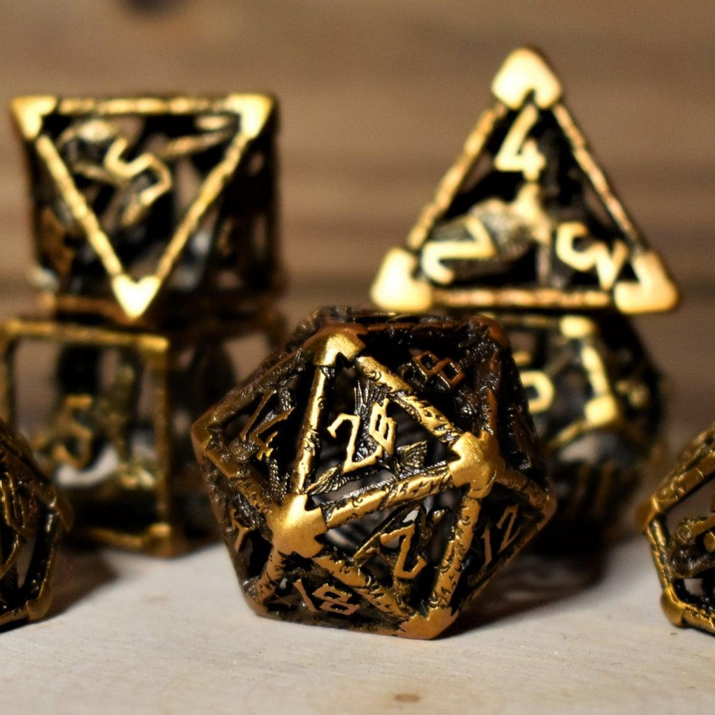 A set of golden brass hollow metal dice with embossed numbers, displayed on a wooden surface.