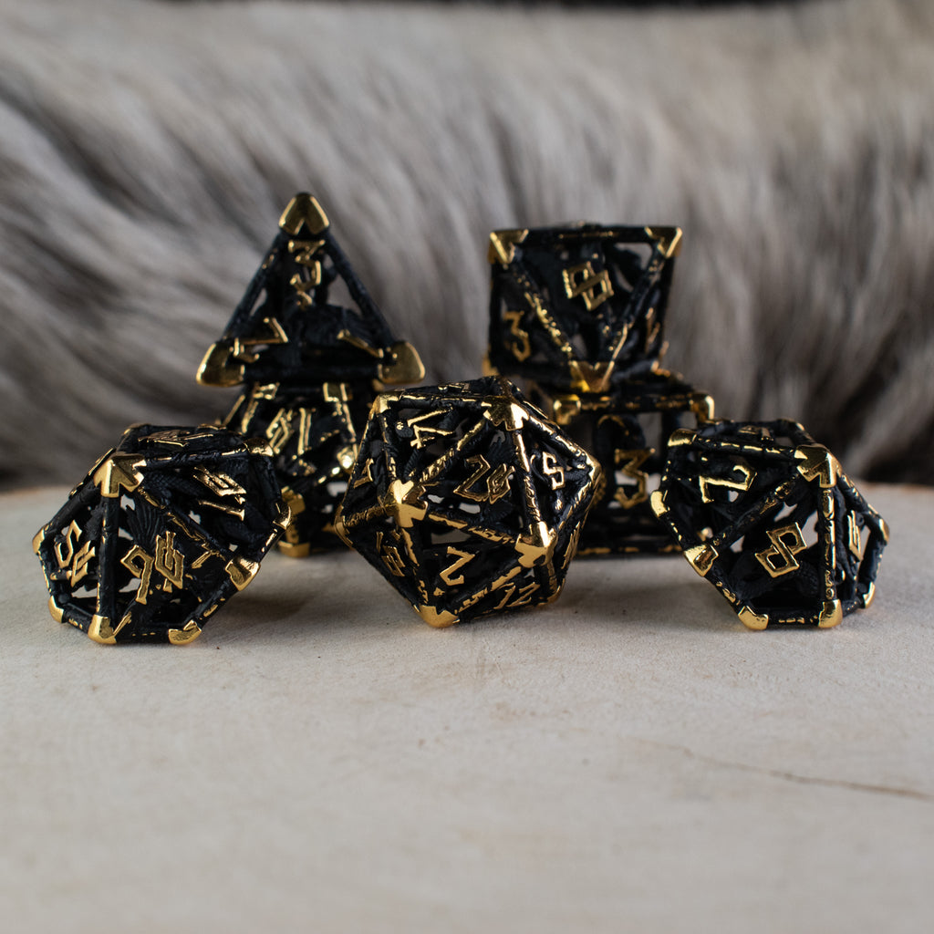 A set of matte black and gold hollow metal dice with embossed numbers, including various shapes such as a d4, d6, d8, d10, d12, and d20, displayed on a white surface.