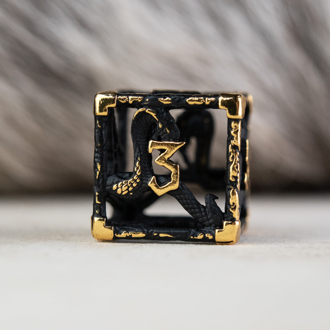 A set of matte black and gold hollow metal dice with embossed numbers, including various shapes such as a d4, d6, d8, d10, d12, and d20, displayed on a white surface.