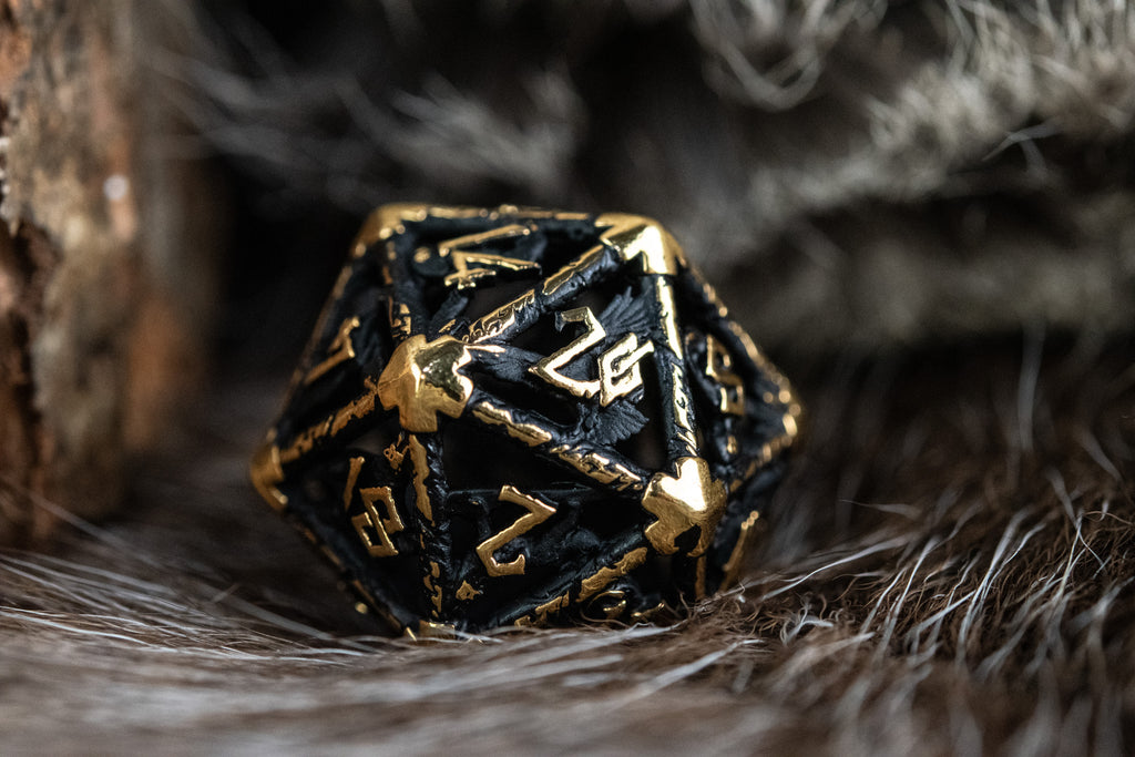 A set of matte black and gold hollow metal dice with embossed numbers, including various shapes such as a d4, d6, d8, d10, d12, and d20, displayed on a white surface.