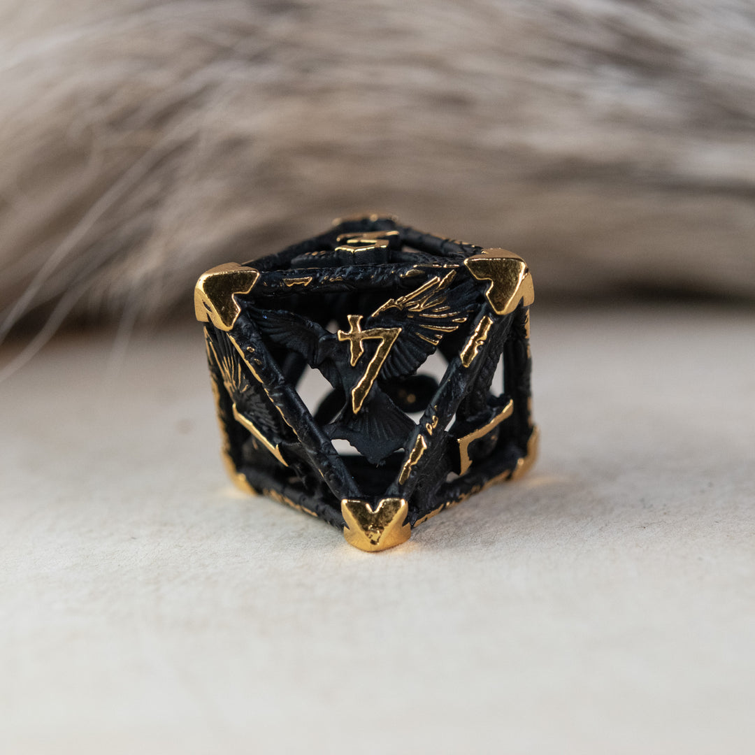 A set of matte black and gold hollow metal dice with embossed numbers, including various shapes such as a d4, d6, d8, d10, d12, and d20, displayed on a white surface.