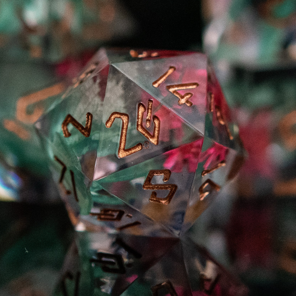 A set of sharp-edged resin dnd dice with bronze hand-painted numbers, featuring green and pink botanicals, reflecting on a shiny surface.
