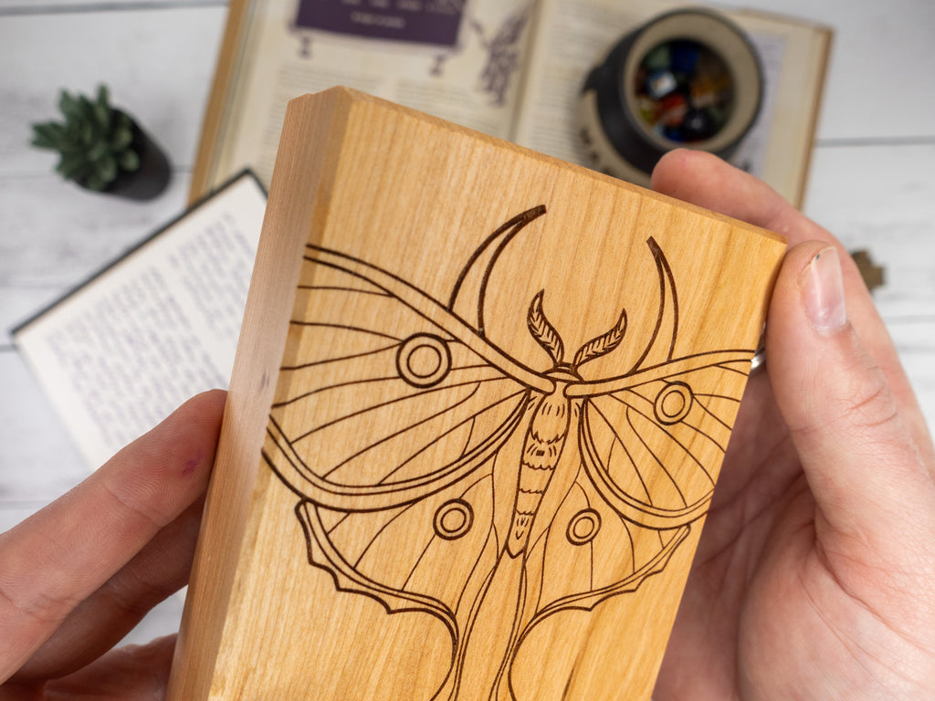 Wooden dice vault with luna moth design held by a hand on a light background