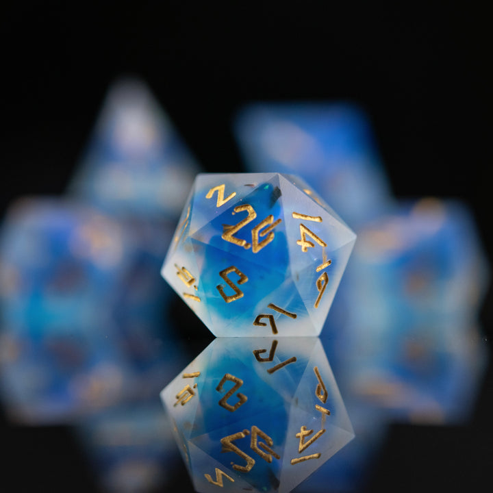 A set of matte blue sharp-edged resin dnd dice with gold engraved numbers, reflecting on a black surface.