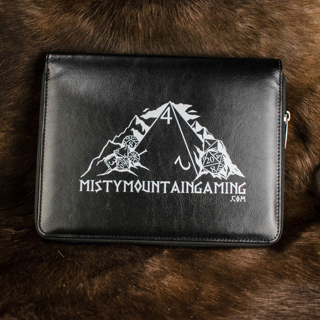 A black poly-leather zippered dice case with foam lining, featuring a white logo 'Mistymountaingaming.com' on the front, placed on a furry surface.