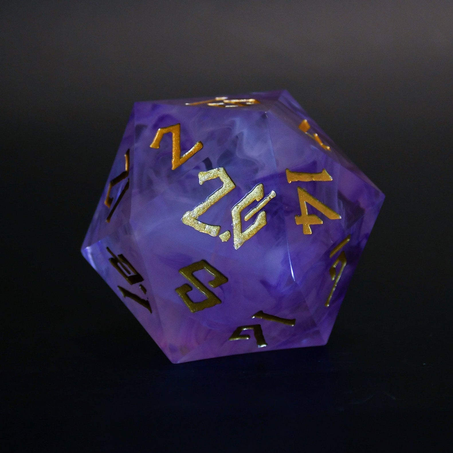 A 50mm purple resin dice with gold engraved numbers, on a dark background.