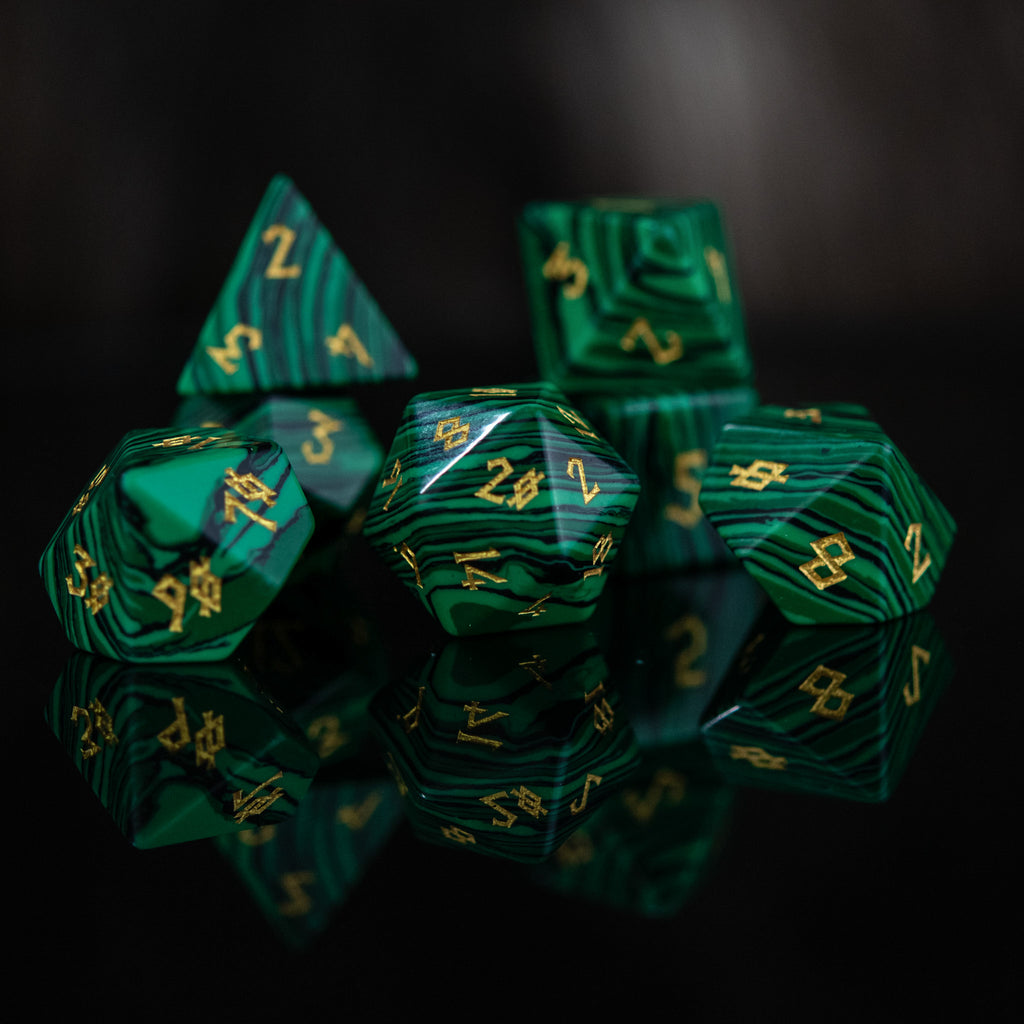 A set of green malachite stone dice with engraved numbers, displayed on a reflective surface.