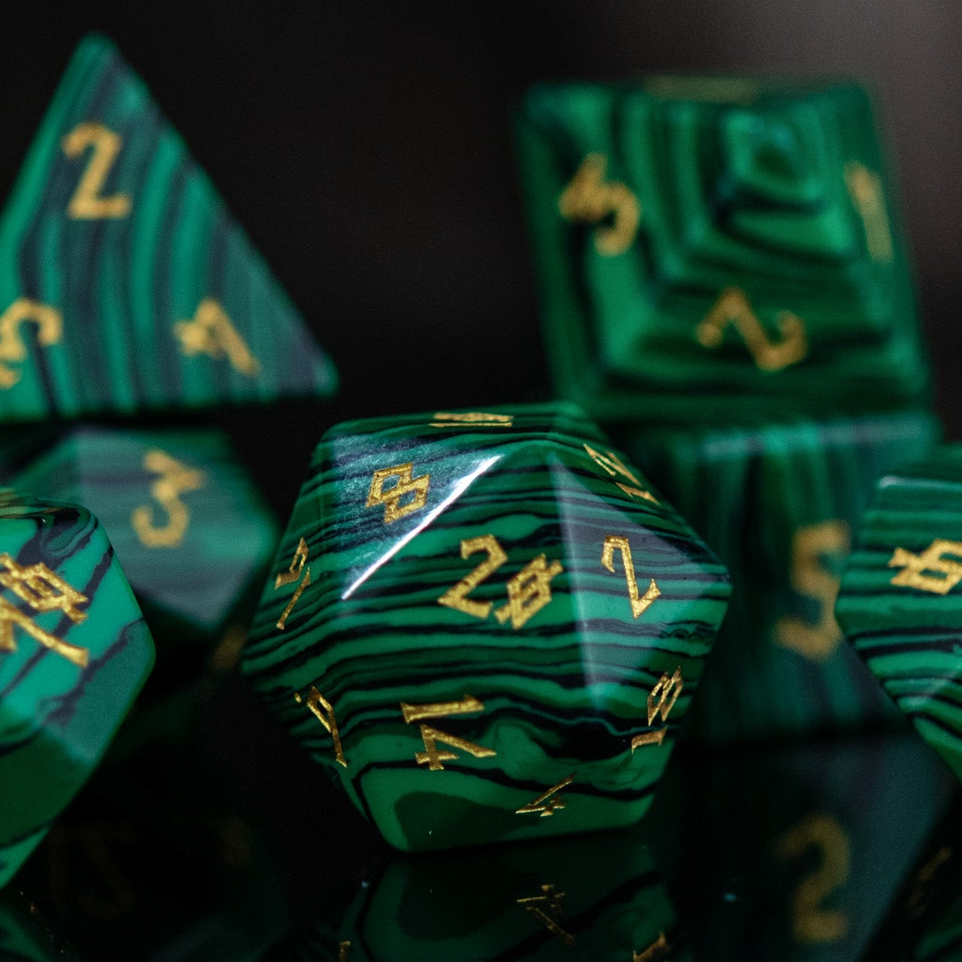 A set of green malachite stone dice with engraved numbers, displayed on a reflective surface.